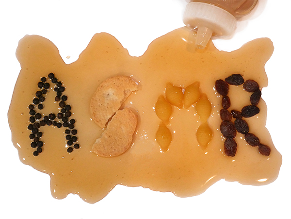 An opaque blob of honey on a white table; "ASMR" is spelled out in pantry staples like pepper seeds, uncooked pasta, raisins and a cookie.